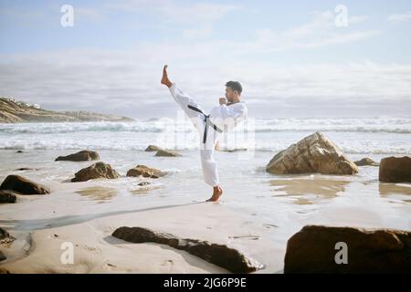 Non ho bisogno di un'arma, io sono uno. Scatto di un giovane artista marziale che pratica il karate sulla spiaggia. Foto Stock