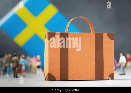 Valigia di cartone, giocattolo di plastica e bandiera su sfondo astratto, un concetto sul tema del trasferimento o migrazione in Svezia Foto Stock