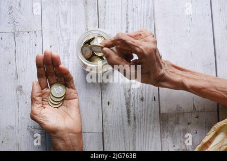 vista dall'alto delle monete a risparmio di mano delle donne anziane in un vaso Foto Stock