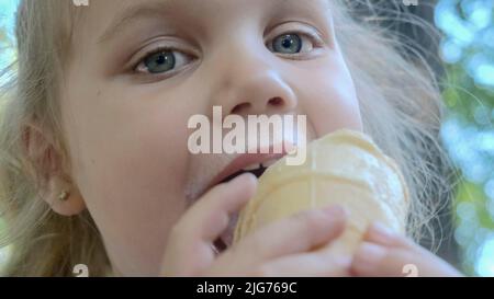 La ragazza piccola carina mangia il gelato fuori. Primo piano ritratto della ragazza bionda seduta sul panchina del parco e mangiare icecream. Odessa Ucraina Foto Stock