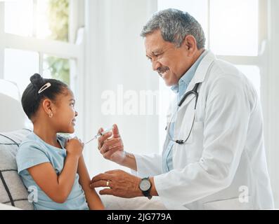 Non vi sentirete una cosa. Shot di un medico maschio maturo che dà una bambina un'iniezione durante un controllo a casa. Foto Stock