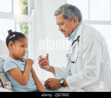 È meglio se si guarda via. Shot di un medico maschio maturo che dà una bambina un'iniezione durante un controllo a casa. Foto Stock