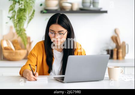 Formazione online, concetto di e-learning. Ragazza asiatica positiva intelligente con occhiali, studente di successo, studiare da casa utilizzando il laptop, ascoltare il webinar online, lezione, prendere appunti, sorridente amichevole Foto Stock