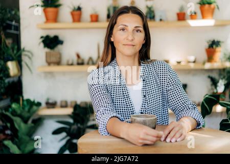 Bella donna brunetta 40s al bar in un negozio accogliente con piante Foto Stock
