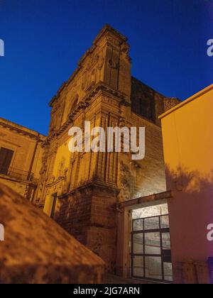 Una chiesa abbandonata con una facciata ornata ma oscurata riflessa dalle luci di strada nelle strade posteriori di Nardo, Puglia al tramonto. Foto Stock