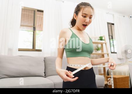 Concetto sano e di perdita di peso, giovane donna asiatica eccitata mentre misurando la vita con metro a nastro. Foto Stock