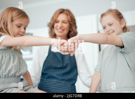 Lascia fare qualcosa di delizioso e fresco. Primo piano sparato di due bambine che si danno un colpo di pugno mentre si cuoce con la loro nonna a casa. Foto Stock