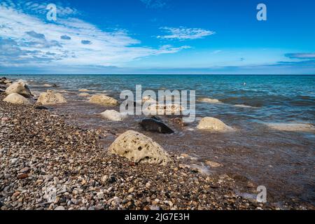 Diversi massi colorati si siedono in acqua lungo la costa rocciosa del lago Michigan sotto un cielo blu nuvoloso nel Wisconsin. Foto Stock