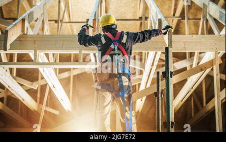 Struttura del telaio della casa di scheletro lavoratore che indossa imbracatura di sicurezza che rimane di fronte all'edificio e si prepara per il lavoro. Foto Stock