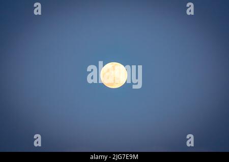 La luna piena si illumina di dettagli contro un cielo blu chiaro Foto Stock