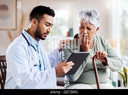 Che sembra serio. Foto di un giovane medico che condivide le informazioni del suo tablet digitale con un paziente più anziano. Foto Stock
