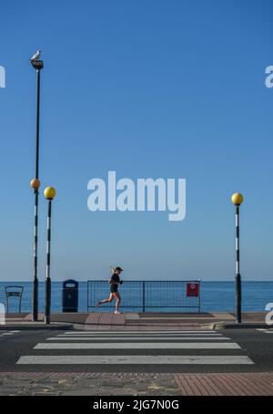 Attraversamento della strada che porta al lungomare e alla spiaggia di Southsea a Portsmouth con un pareggiatore che corre oltre. Foto Stock