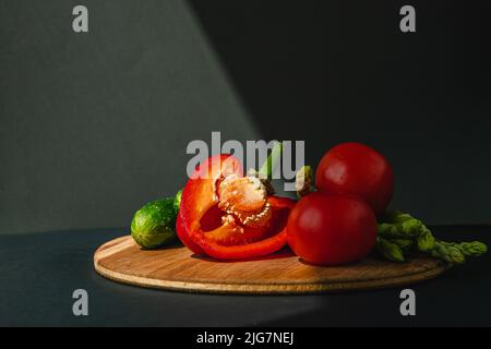 rami di asparagi verdi freschi, peperoni, pomodori e cetrioli su un asse di legno, sfondo grigio scuro, vista dall'alto. Concetto di tendenza di base con spazio di copia Foto Stock