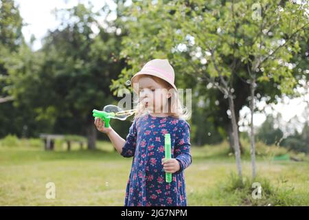 Carino ragazza piccola che soffia le bolle di sapone su una passeggiata in estate all'aperto Foto Stock