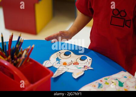 Un bambino piccolo che colora una maschera di carta animale in classe. Unicorn carta maschera arti e mestieri. Khobar, Arabia Saudita. Foto Stock