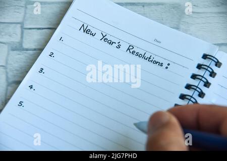 Scrivere a mano il testo delle risoluzioni del nuovo anno su blocco note. Il concetto di risoluzione del nuovo anno Foto Stock