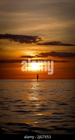 Una silhouette di un uomo pagaia a bordo del mare durante un tramonto panoramico Foto Stock