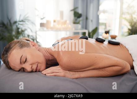 Permette di annullare gli effetti dello stress cronico sul vostro corpo. Shot di una donna matura che gode di un rilassante massaggio con pietre calde in una spa. Foto Stock