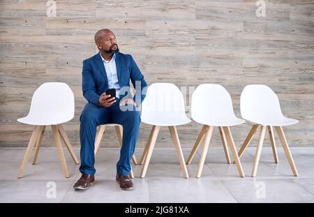 Il successo è un'opportunità. Scatto di un uomo d'affari maturo che usa un telefono mentre aspetta in linea ad un ufficio. Foto Stock