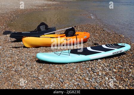 Tre canoe riposano sul bordo della spiaggia di ghiaia alla foce del fiume Ax in Axmouth Foto Stock