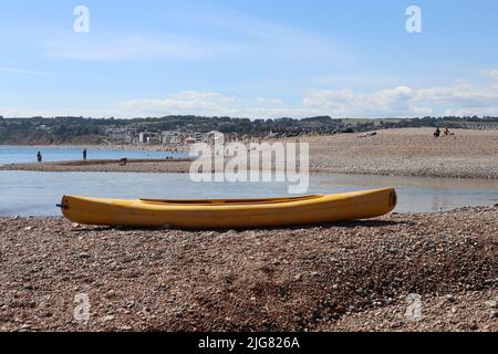 Una canoa gialla si trova sulla cima di una riva di ghiaia alla foce del fiume Ax in Axmouth Foto Stock