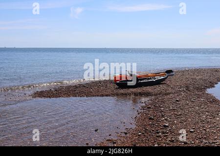 Tre canoe riposano sul bordo della spiaggia di ghiaia alla foce del fiume Ax in Axmouth Foto Stock