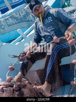 Hurghada, Egitto - 21 febbraio 2022: Pescatore cucire reti da pesca nel porto egiziano Foto Stock