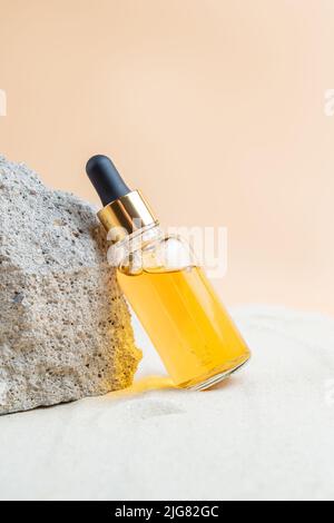 Flacone contagocce di idratante, siero o olio di vitamina C per il viso su pietre con sabbia, fondo di sabbia, trattamento del viso estivo. Foto Stock