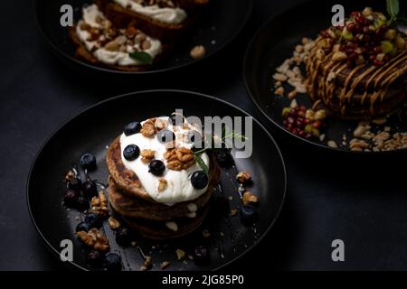 Colazione perfetta, pancake americani accatastati serviti su un tavolo di pietra nera. Deliziose frittelle americane impilate con mirtillo, da vicino, vista dall'alto. Foto Stock