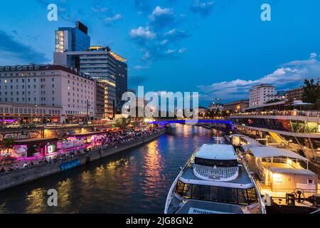 Vienna, fiume Donaukanal (canale del Danubio), persone sedute sul rinforzo della sponda, ristoranti e bar all'aperto, terminal delle barche Schwedenplatz, hotel Sofitel nel 01. Quartiere Città Vecchia, Vienna, Austria Foto Stock