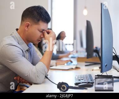 Dacci un taglio. Scatto di un giovane agente del call center che osserva stressato mentre lavora in ufficio. Foto Stock