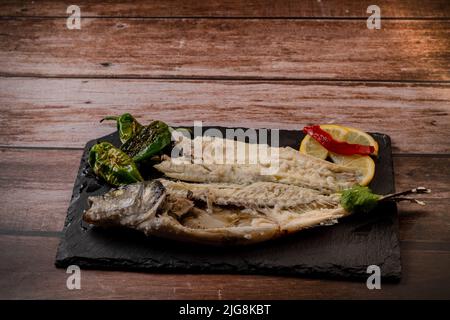 spigola fresca cotta in sale su ardesia nera, con limone e peperoni verdi e rossi Foto Stock
