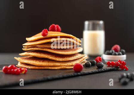 Mini pancake con mirtilli e lamponi. Colazione all'americana su sfondo scuro. Alimentazione sana per tutta la famiglia. Pancake fatti in casa con Foto Stock