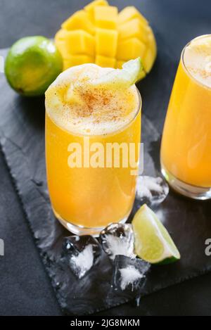 Succo di mango su sfondo scuro. Drink estivo con ghiaccio e fettine di mango e lime. Foto Stock