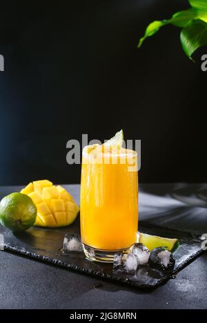 Cocktail mango estivo giallo brillante. Fette di mango e lime su sfondo nero. Drink di stagione. Cocktail per vegetariani e per coloro che seguono una dieta Foto Stock