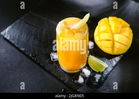 Nettare di succo di mango e lime. Un drink estivo rinfrescante su sfondo nero. Colori giallo chiaro e nero Foto Stock