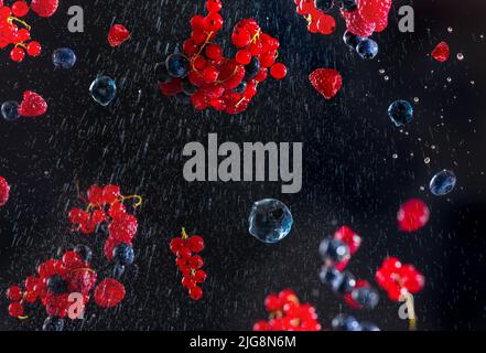 Bacche fresche su sfondo blu nero con gocce d'acqua che volano in direzioni diverse. Molti bacche diversi nella forma di una cornice su un buio Foto Stock