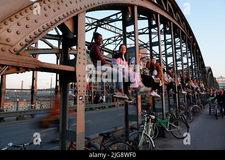 Germania, Baviera, Monaco, Haccurbrücke, giovani si siedono sulla costruzione del ponte e godersi il tramonto Foto Stock