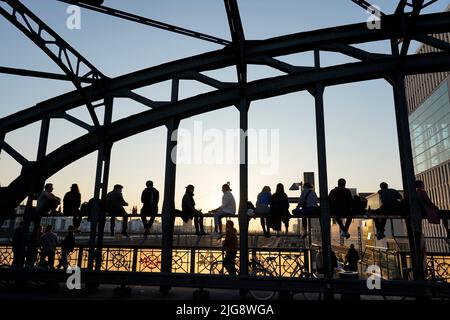 Germania, Baviera, Monaco, Haccurbrücke, giovani si siedono sulla costruzione del ponte e godersi il tramonto Foto Stock