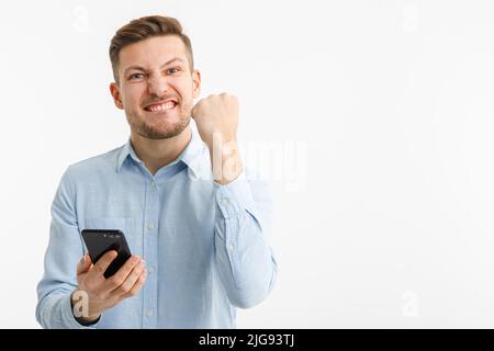 Un uomo tiene uno smartphone in mano e si rallegra di una transazione di successo sugli scambi cripto. Isolato su sfondo bianco. Foto Stock