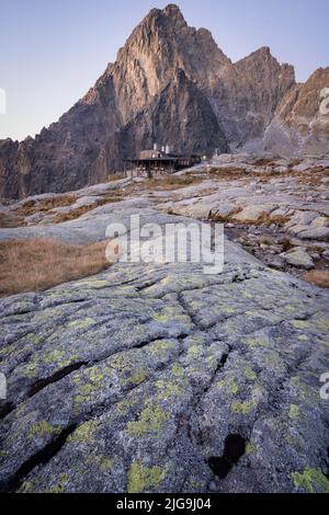 Capanna alpina situata sotto un picco roccioso al mattino presto, colpo verticale, Slovacchia, Europa Foto Stock