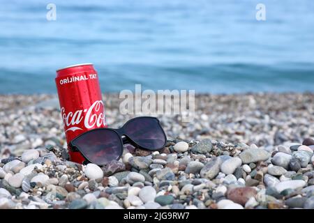 ANTALYA, TURCHIA - 18 MAGGIO 2021: L'originale lattina rossa Coca Cola si trova su piccole pietre di ciottoli rotonde vicino al mare. Coca-cola lattina e occhiali da sole su t Foto Stock