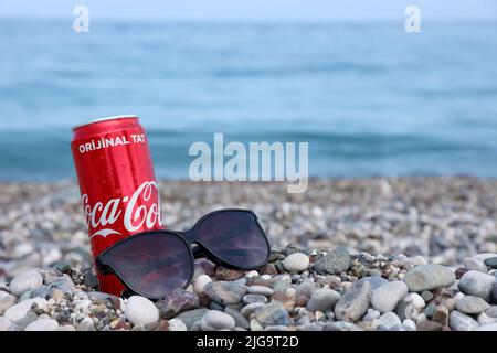 ANTALYA, TURCHIA - 18 MAGGIO 2021: L'originale lattina rossa Coca Cola si trova su piccole pietre di ciottoli rotonde vicino al mare. Coca-cola lattina e occhiali da sole su t Foto Stock