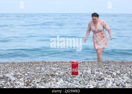 ANTALYA, TURCHIA - 18 MAGGIO 2021: L'originale lattina rossa Coca Cola si trova su piccole pietre di ciottoli rotonde vicino al mare. Coca-cola può e donna su turkis Foto Stock