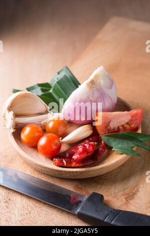 verdure, ingredienti aromatizzanti comuni per la cucina asiatica e sud-asiatica, erbe e spezie per cucinare su un piatto di legno con un coltello Foto Stock