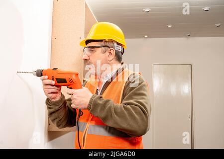 Operatore vestito con giubbotto di sicurezza uniforme, casco e occhiali di sicurezza, forando una parete con un trapano. Concetto di lavoro, costruttore, lavoratore. Foto Stock