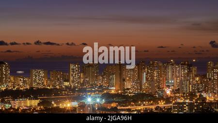 Alti grattacieli illuminati di notte in una città con piccole case in primo piano notte splendidi edifici moderni e luci luminose. Il Foto Stock