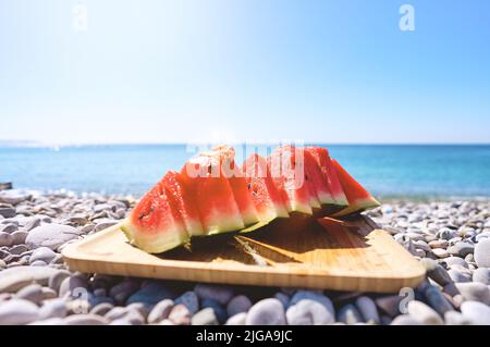Succose fette di cocomero sul piatto. Sullo sfondo il mare e la spiaggia. Cocomero rosso, frutta fresca. Ora legale. Foto Stock