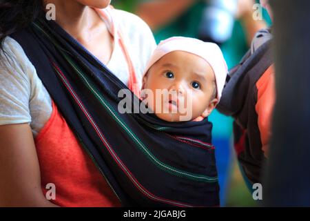 Le donne di minoranza etnica trasportano i loro bambini con le grandi sciarpe Foto Stock