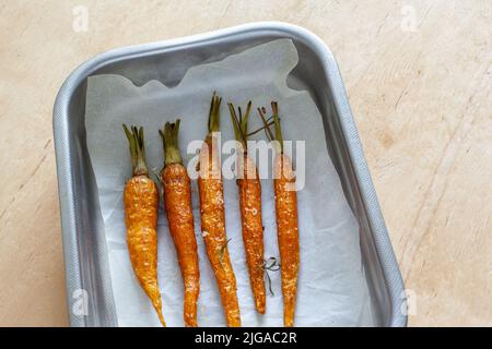 Carota intera giovane arrosto con verdure e sale marino in teglia da forno Foto Stock